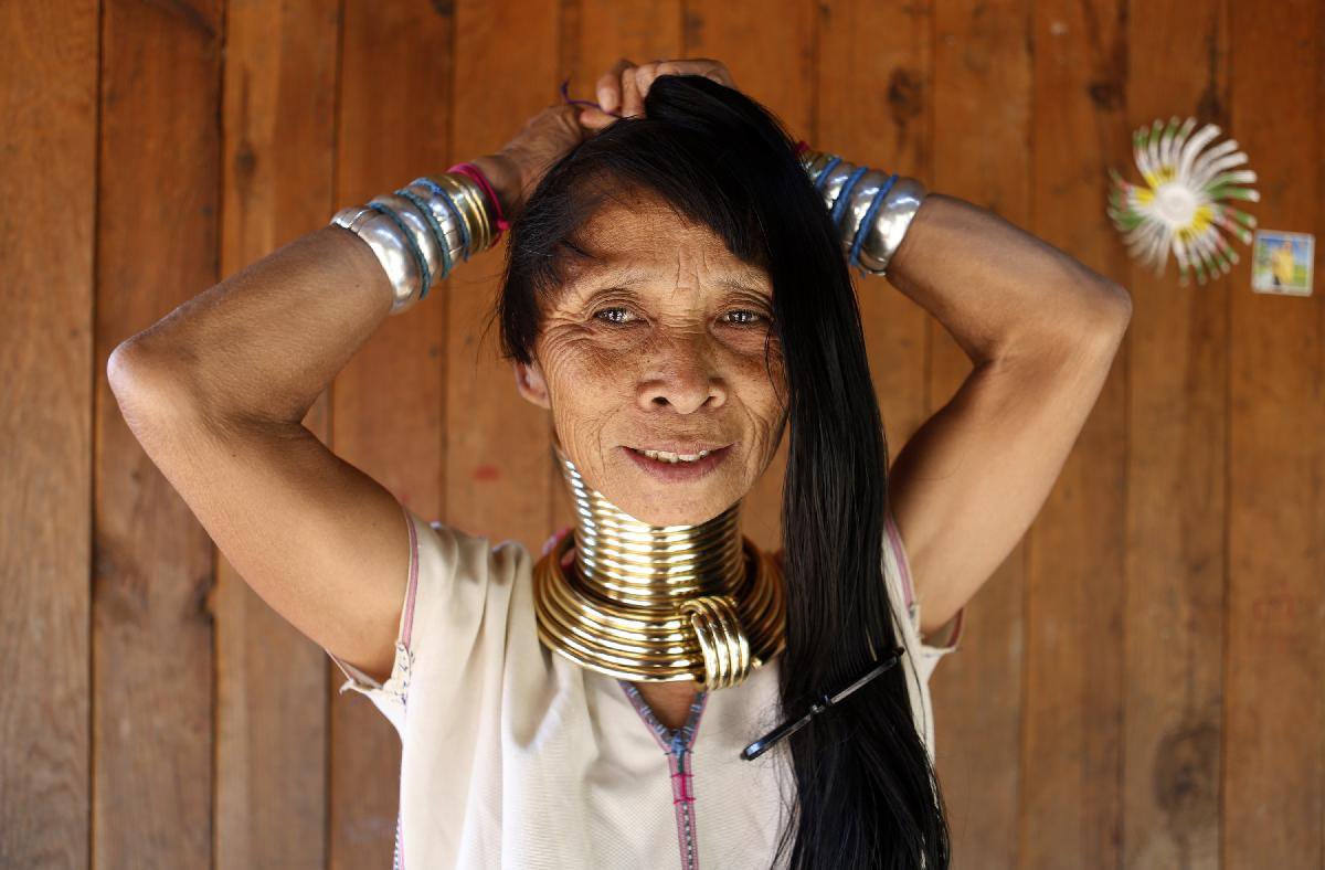 A Padaung woman with brass rings around her neck combs her hair at her home...